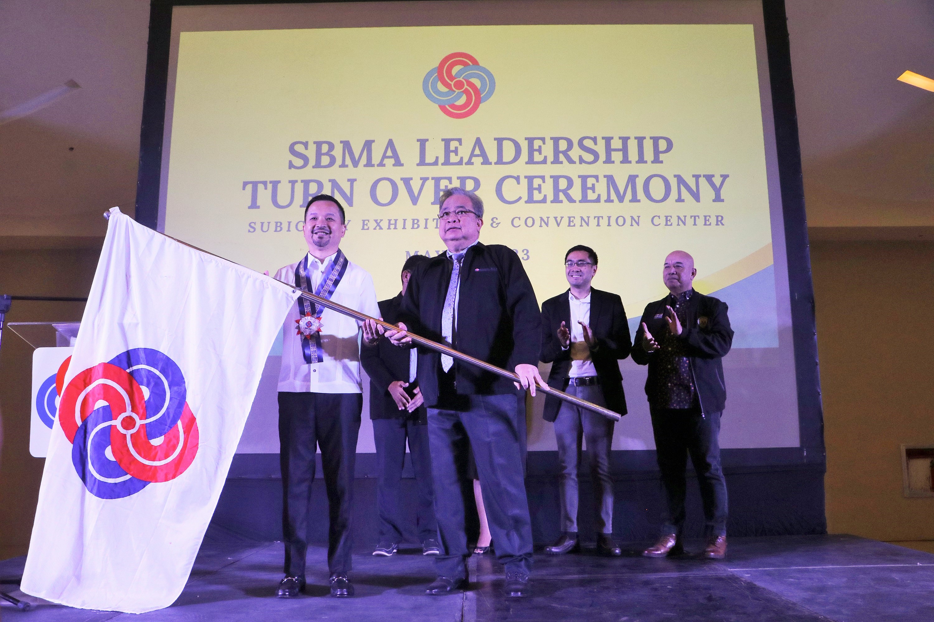 Newly appointed Subic Bay Metropolitan Authority (SBMA) Chairman &amp; Administrator Jonathan D. Tan symbolically receives the leadership of the agency from the Board of Directors headed by Atty. Tomas Lahom III, who hands over the agency flag during a modest turnover ceremony on Tuesday, May 16, 2023 at the Subic Bay Exhibition &amp; Convention Center (SBECC).